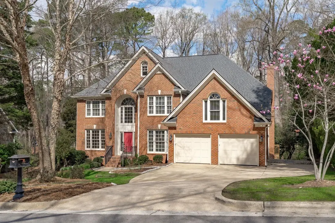 1990s red brick colonial with white trim, gray roof, cream garage doors and a red front door