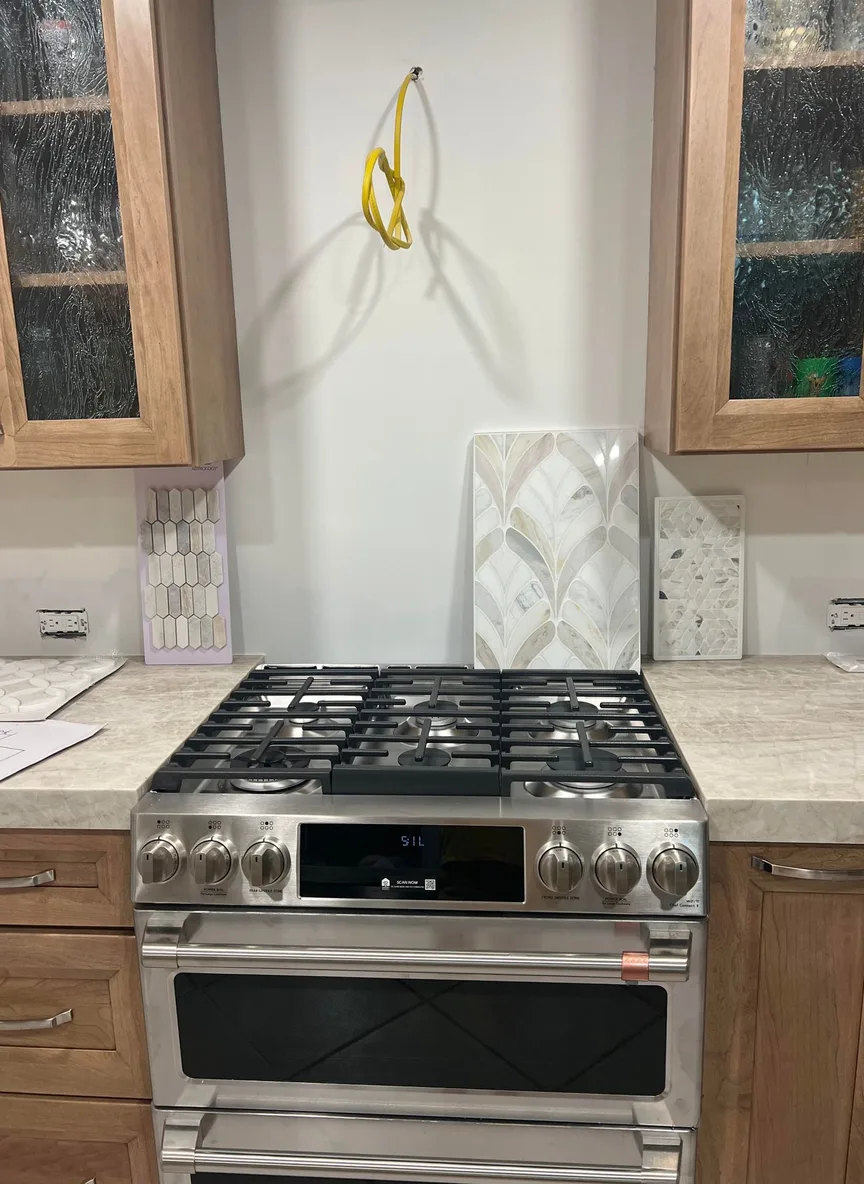 Honey oak kitchen cabinets with cream stone countertops and tile samples propped against a bare backsplash wall