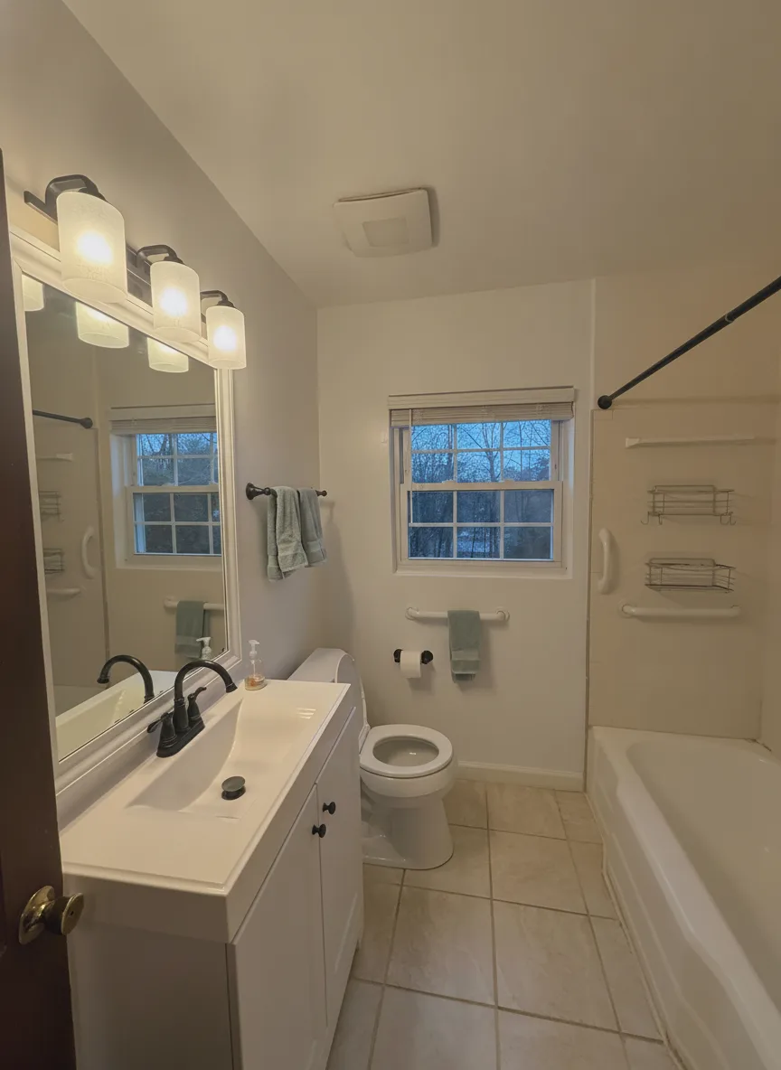 The same dated bathroom with only the yellow walls repainted soft warm white, vanity, tile and fixtures unchanged